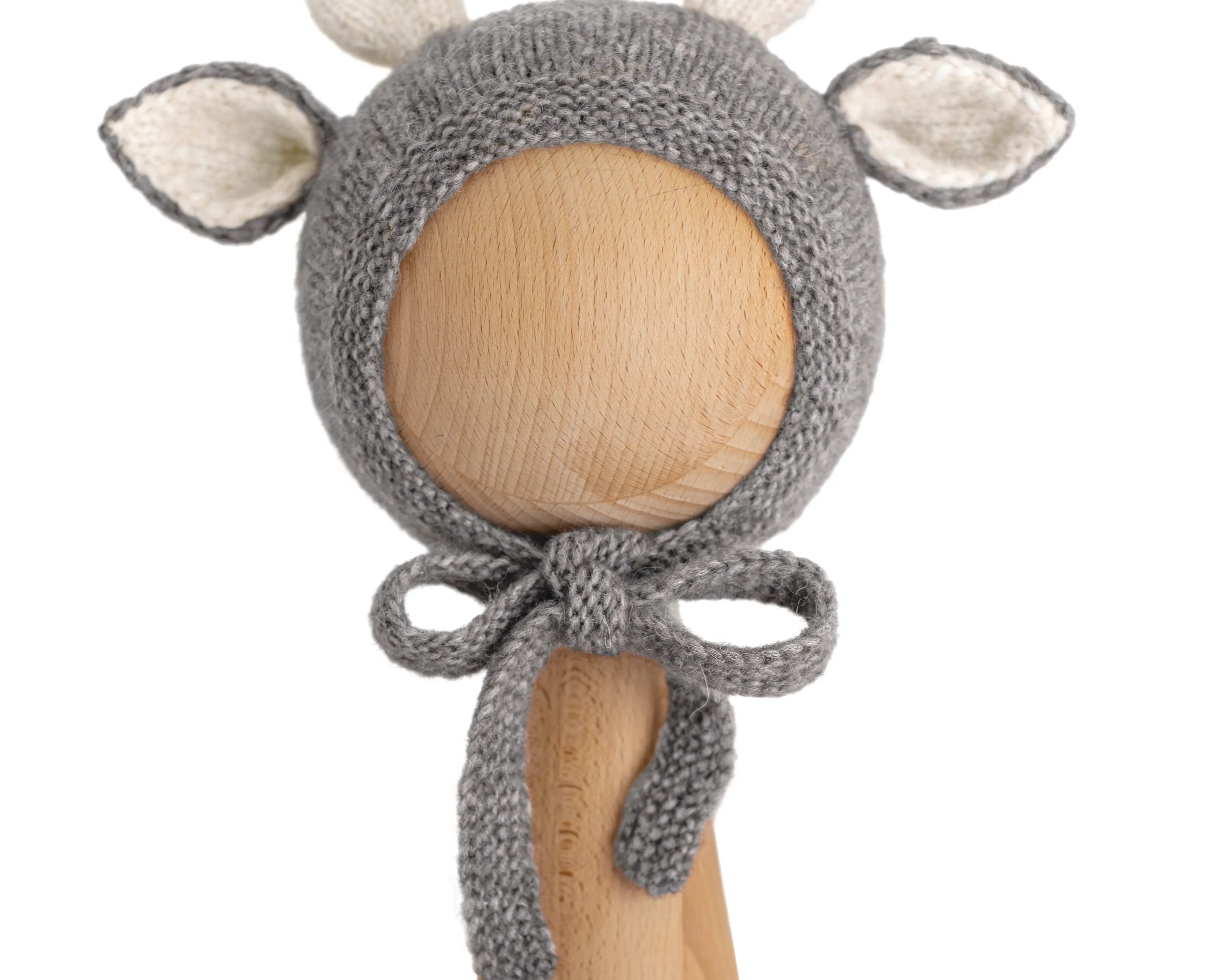 A gray knitted baby bonnet with antler and ear details, displayed on a wooden mannequin head against a plain white background.