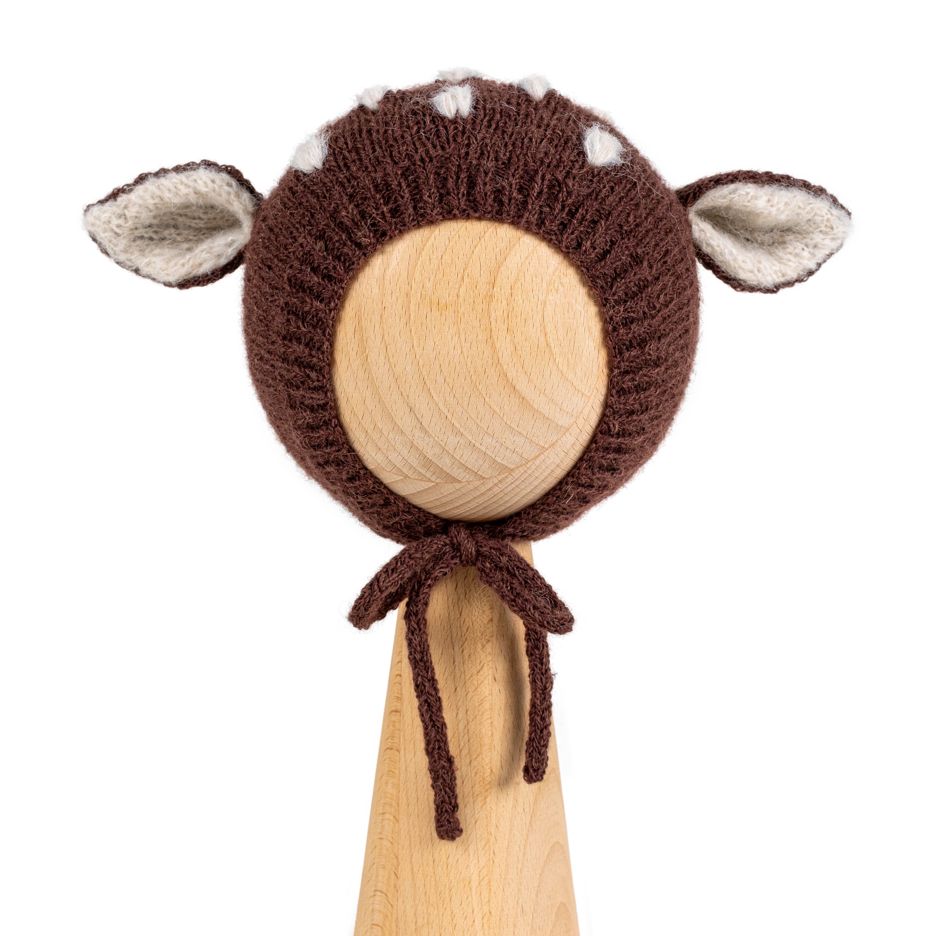 Brown knitted baby bonnet with deer ears and white spots in Hot Chocolate, shown on a wooden display head.