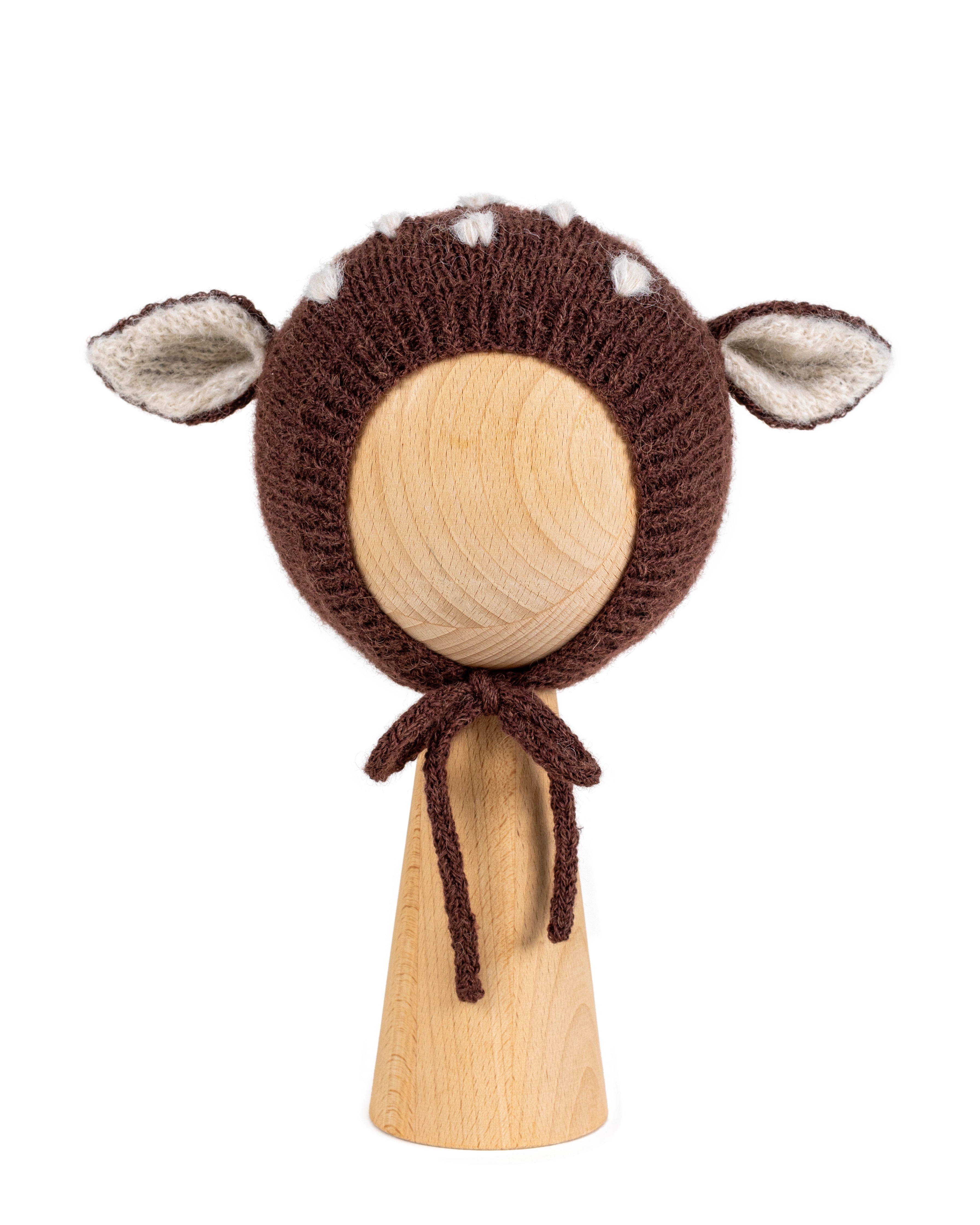 Brown knitted baby bonnet with deer ears and white spots in Hot Chocolate, shown on a wooden display head.