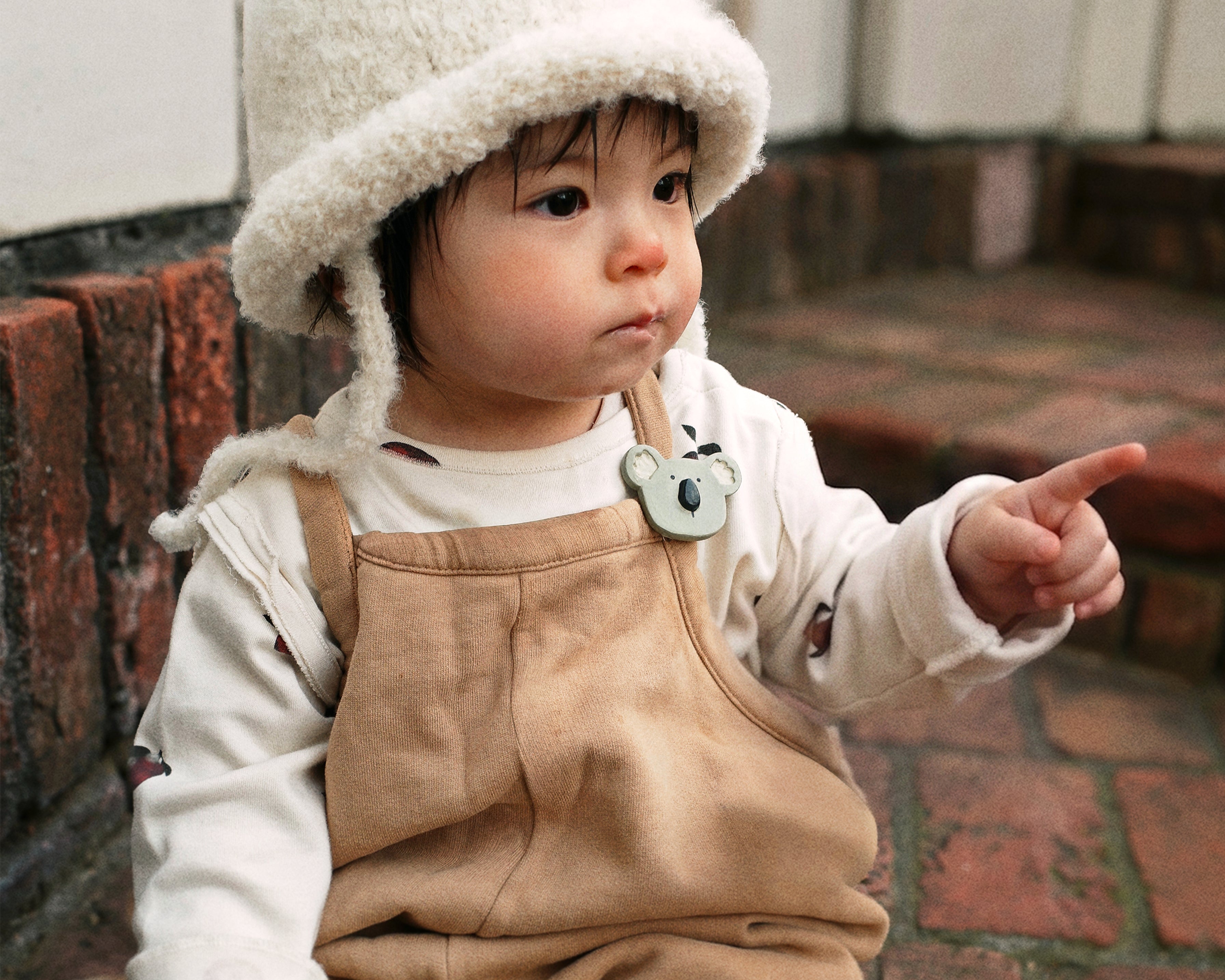 A toddler wearing the Bucket Bear Hat, a knitted bucket hat with bear ears, from the Gang of Kids winter collection.
