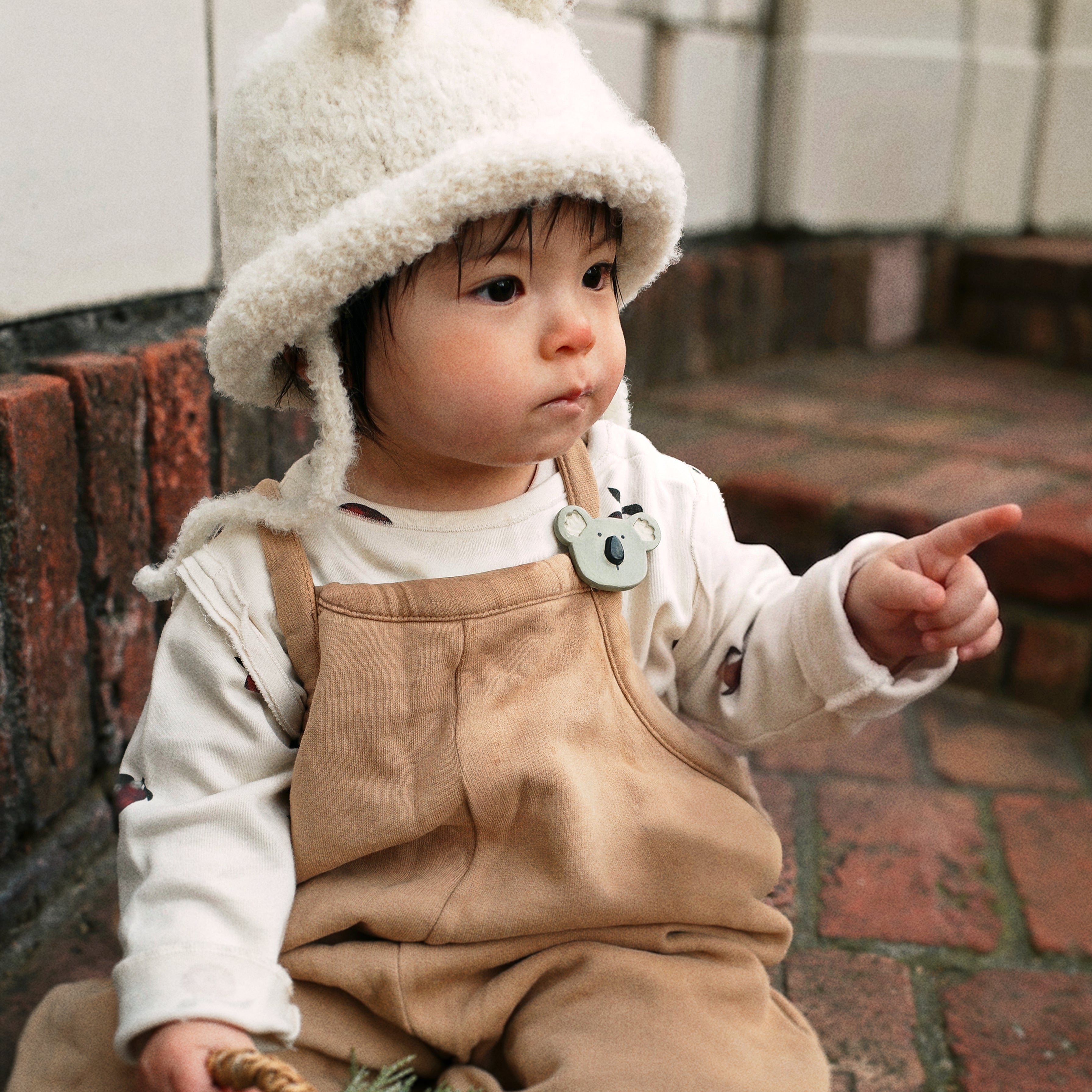 A toddler wearing the Bucket Bear Hat, a knitted bucket hat with bear ears, from the Gang of Kids winter collection.