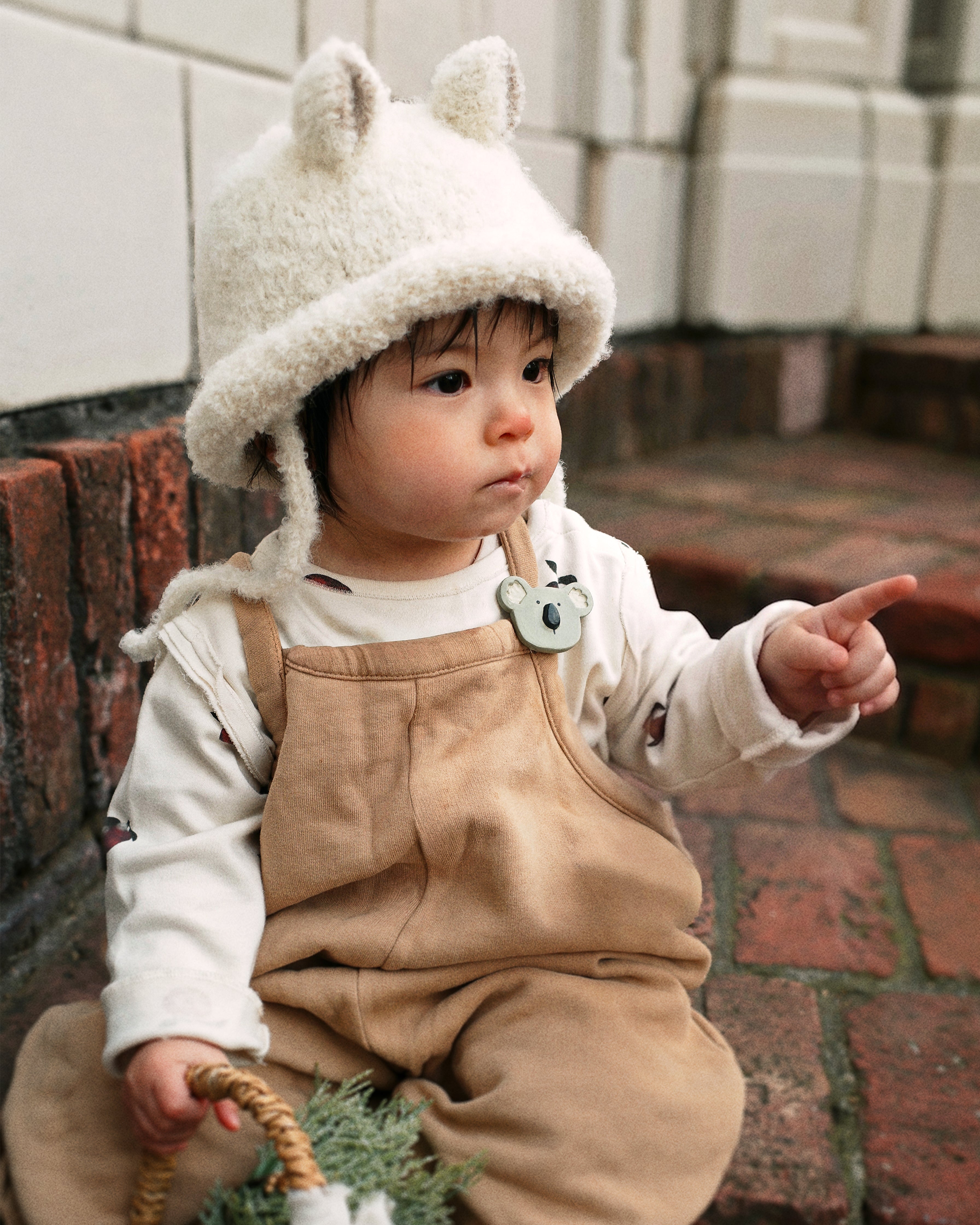 A toddler wearing the Bucket Bear Hat, a knitted bucket hat with bear ears, from the Gang of Kids winter collection.