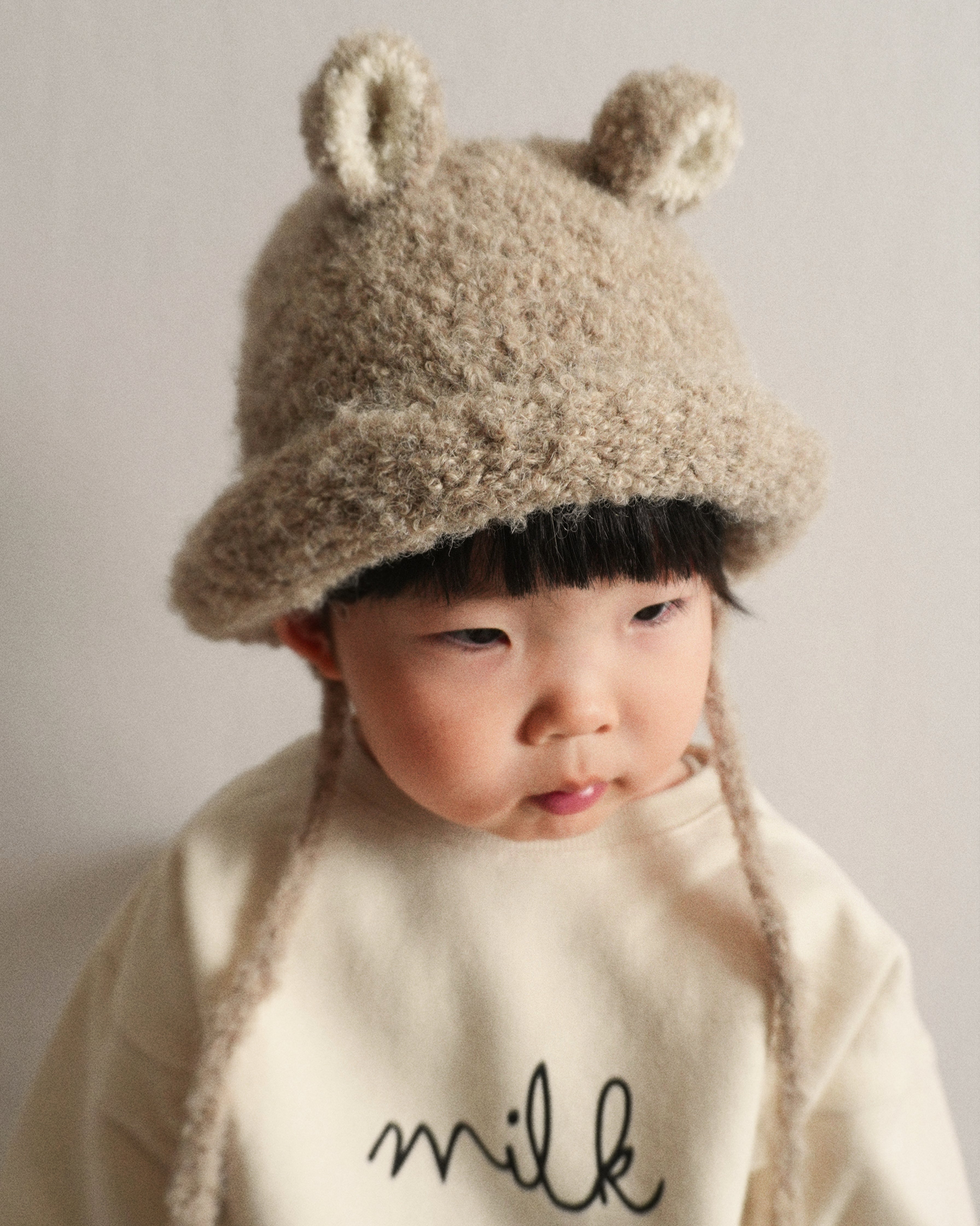 A portrait of a child wearing the Bucket Bear Hat in beige, a knitted bucket hat with bear ears, from the Gang of Kids winter collection.