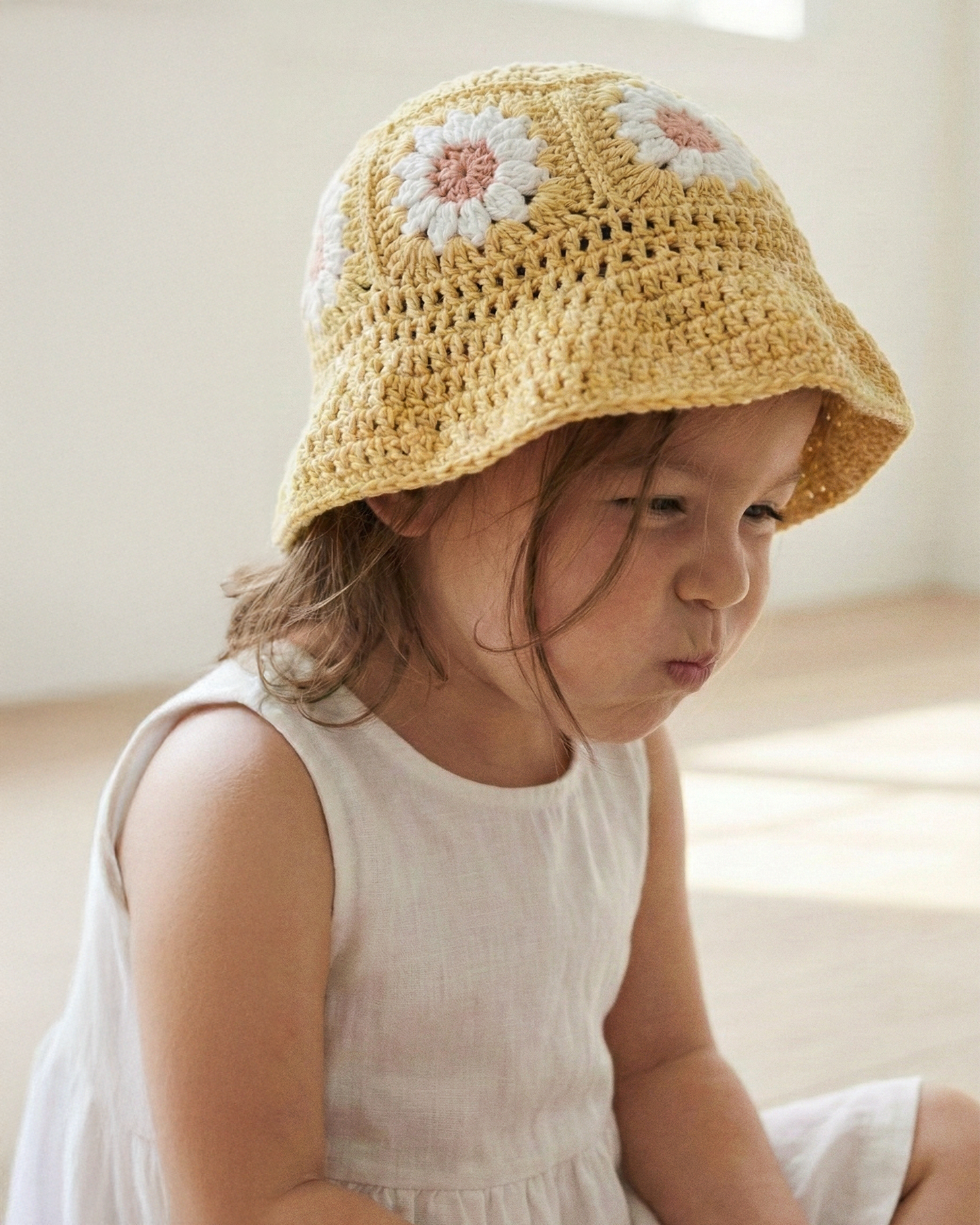 Dziewczynka w żółtym szydełkowym kapeluszu Daisy Buttercup Yellow w białej sukience | Girl wearing yellow Daisy crocheted toddler sun hat in white dress