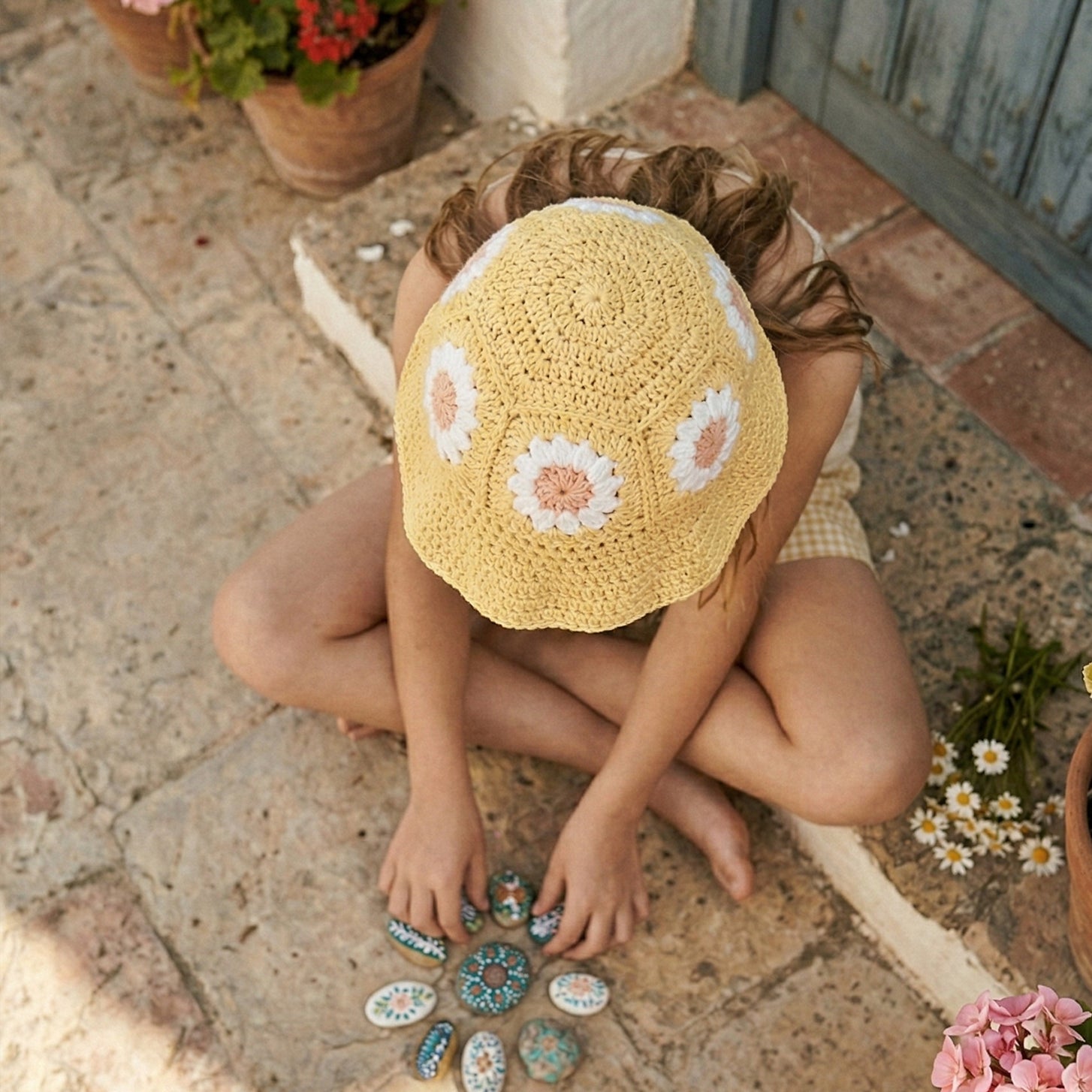 Widok z góry na żółty szydełkowy kapelusz dziecięcy Daisy z różowymi stokrotkami | Top view of yellow Daisy crocheted toddler hat with pink daisy flowers
