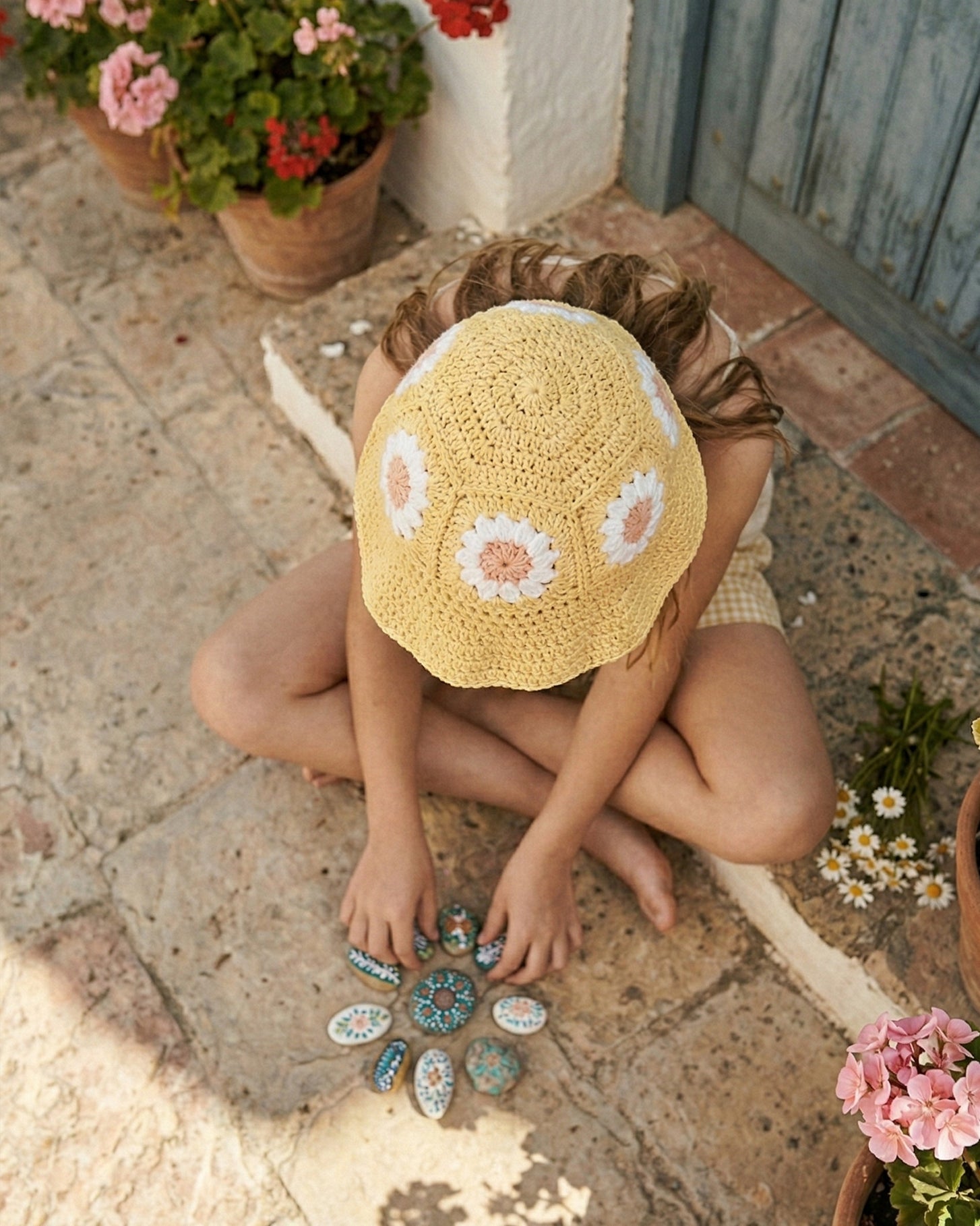 Widok z góry na żółty szydełkowy kapelusz dziecięcy Daisy z różowymi stokrotkami | Top view of yellow Daisy crocheted toddler hat with pink daisy flowers
