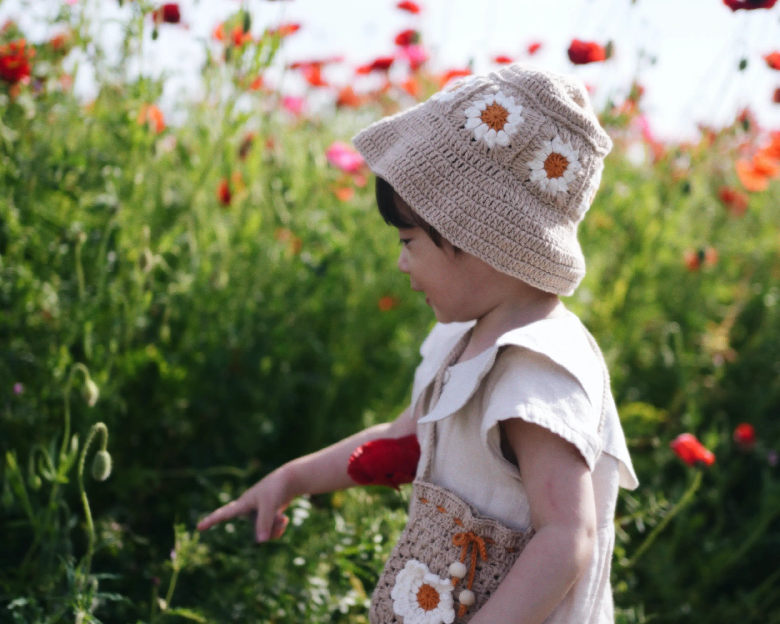 Dziecko w beżowym szydełkowym kapeluszu Daisy Sand Dune na polu czerwonych maków | Toddler wearing beige Daisy crocheted sun hat in red poppy field