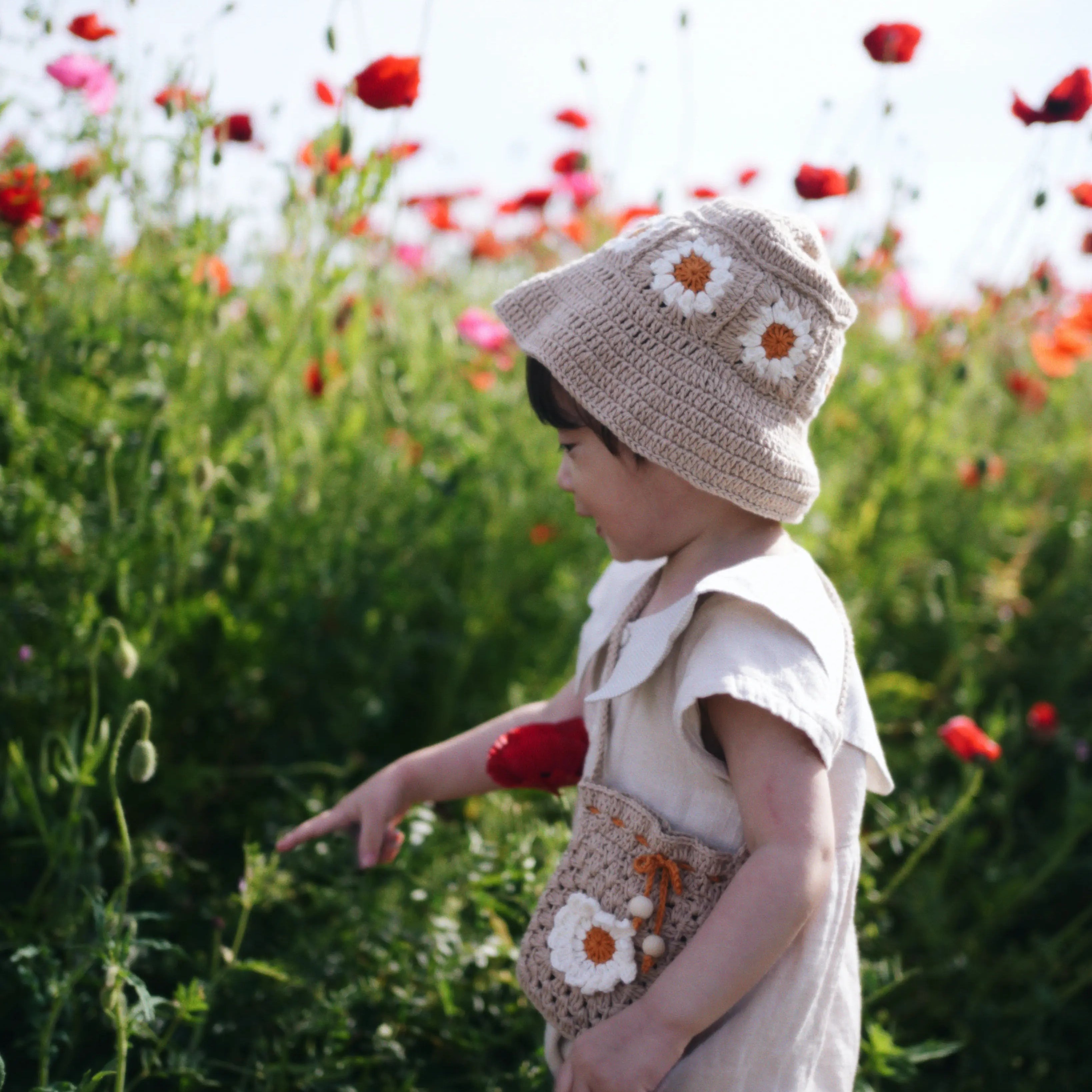Dziecko w beżowym szydełkowym kapeluszu Daisy Sand Dune na polu czerwonych maków | Toddler wearing beige Daisy crocheted sun hat in red poppy field