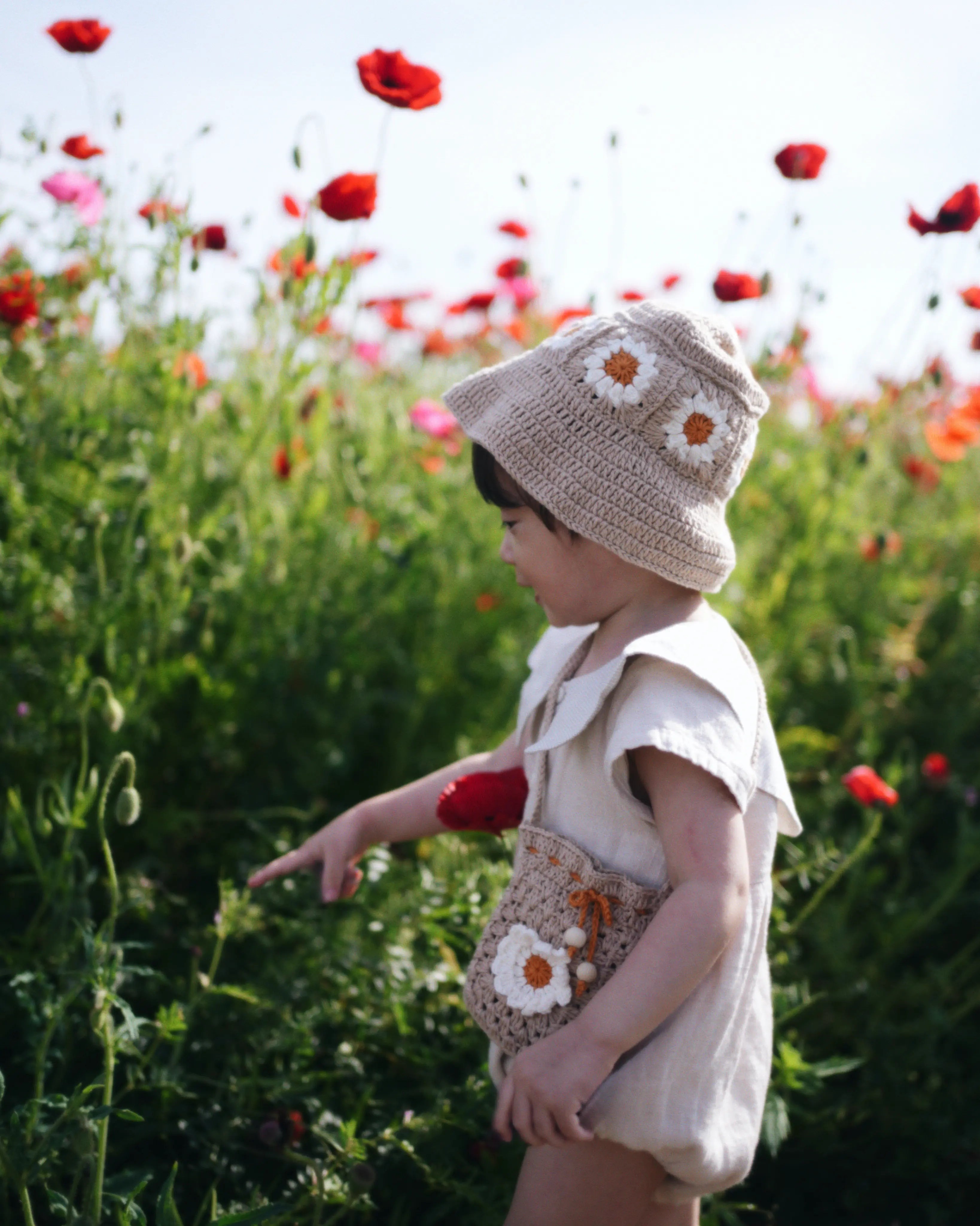 Dziecko w beżowym szydełkowym kapeluszu Daisy Sand Dune na polu czerwonych maków | Toddler wearing beige Daisy crocheted sun hat in red poppy field