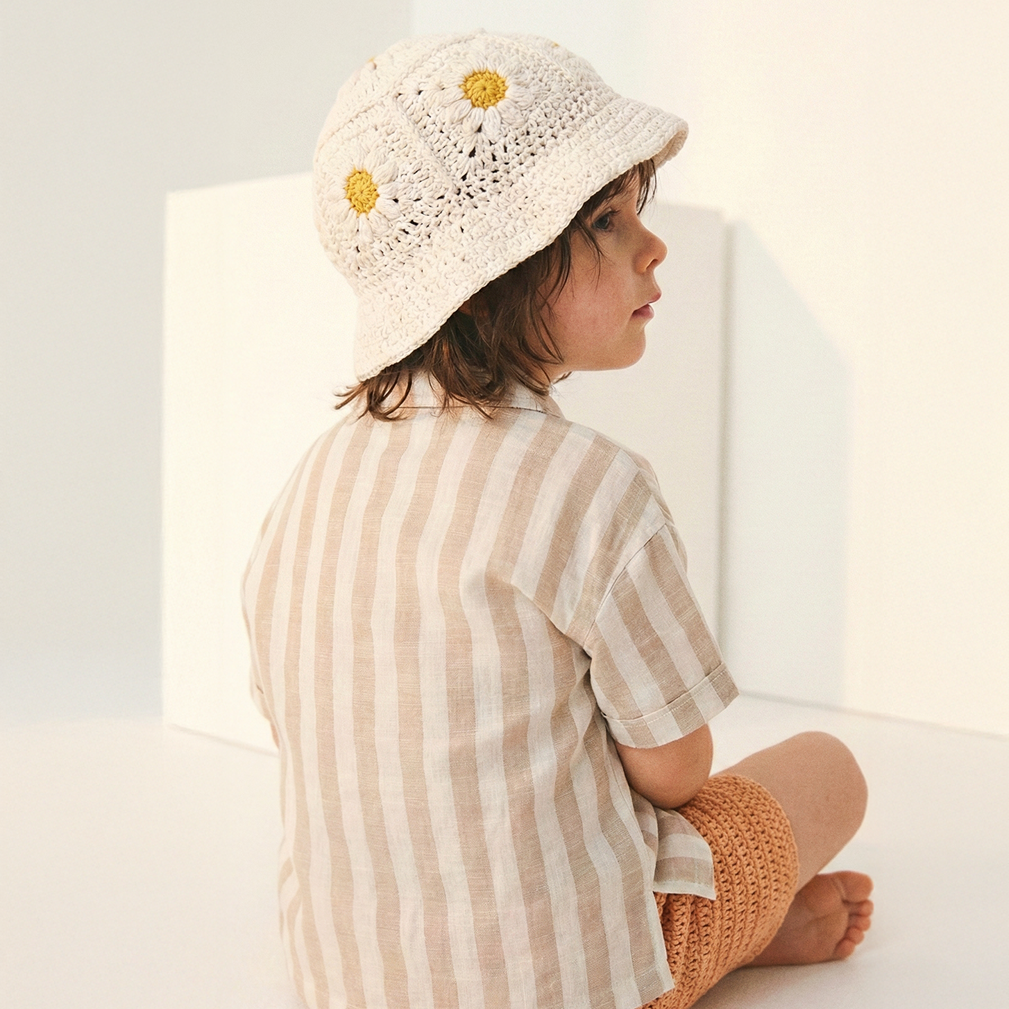Dziecko od tyłu w kremowym szydełkowym kapeluszu Daisy z żółtymi stokrotkami | Toddler from behind wearing Daisy Vanilla Cream crochet hat with yellow daisy flowers