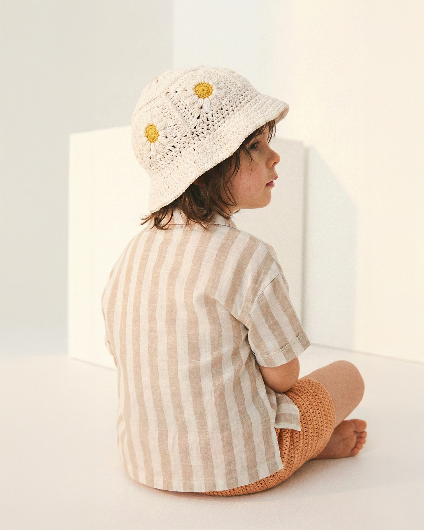 Dziecko od tyłu w kremowym szydełkowym kapeluszu Daisy z żółtymi stokrotkami | Toddler from behind wearing Daisy Vanilla Cream crochet hat with yellow daisy flowers