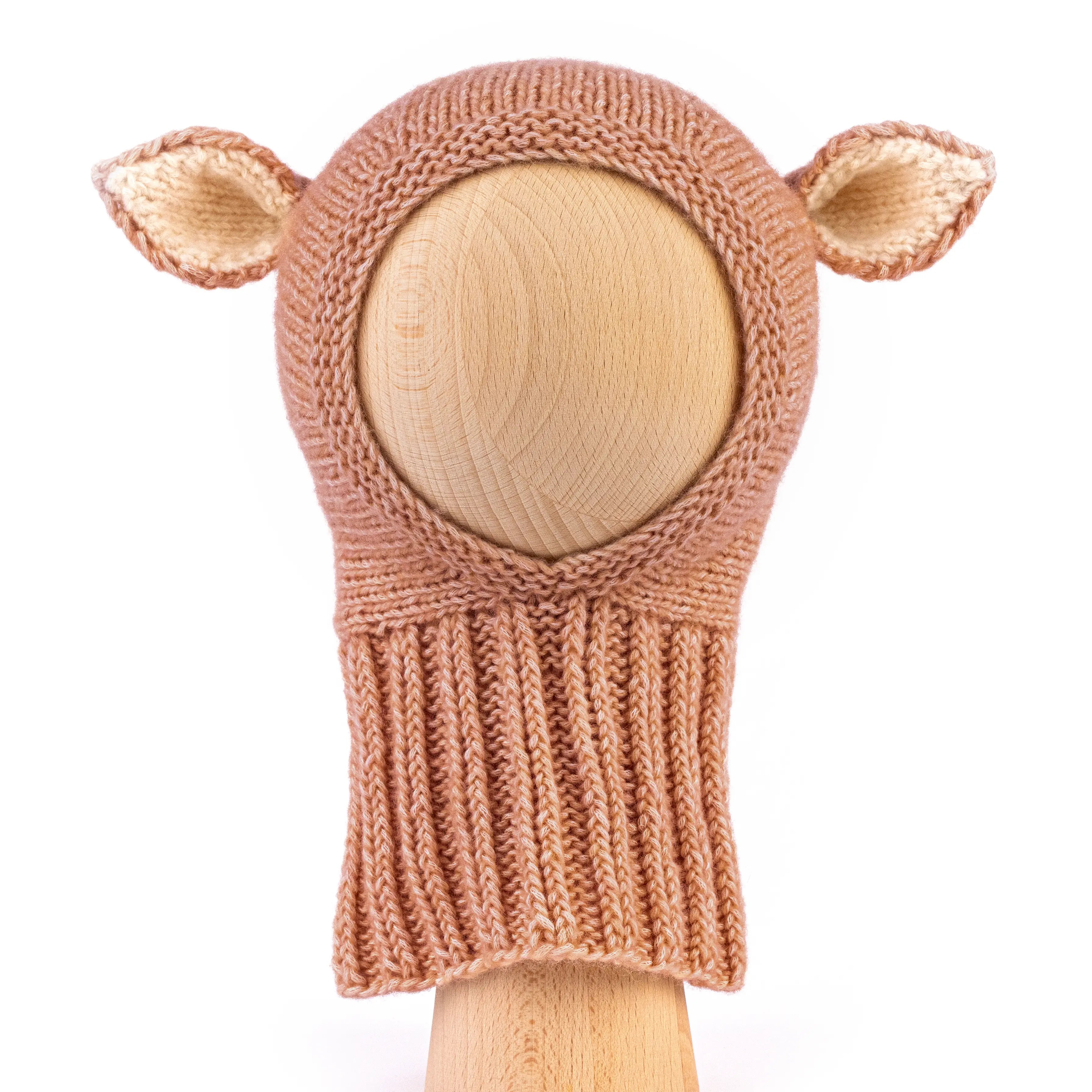 A hand-knit baby hat in a warm tan color, featuring two small pointed ears on the sides, displayed on a light wood mannequin head against a white background.