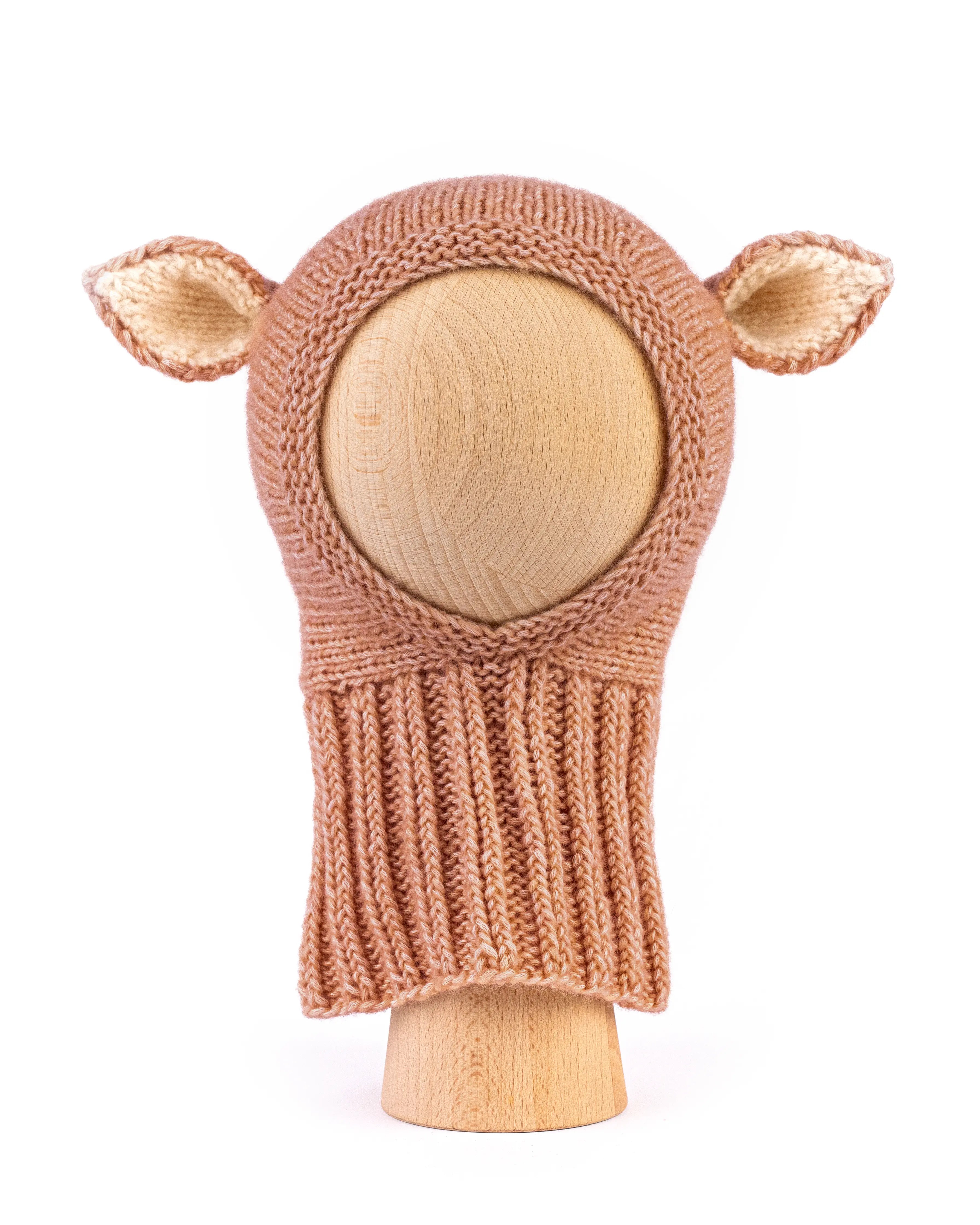 A hand-knit baby hat in a warm tan color, featuring two small pointed ears on the sides, displayed on a light wood mannequin head against a white background.