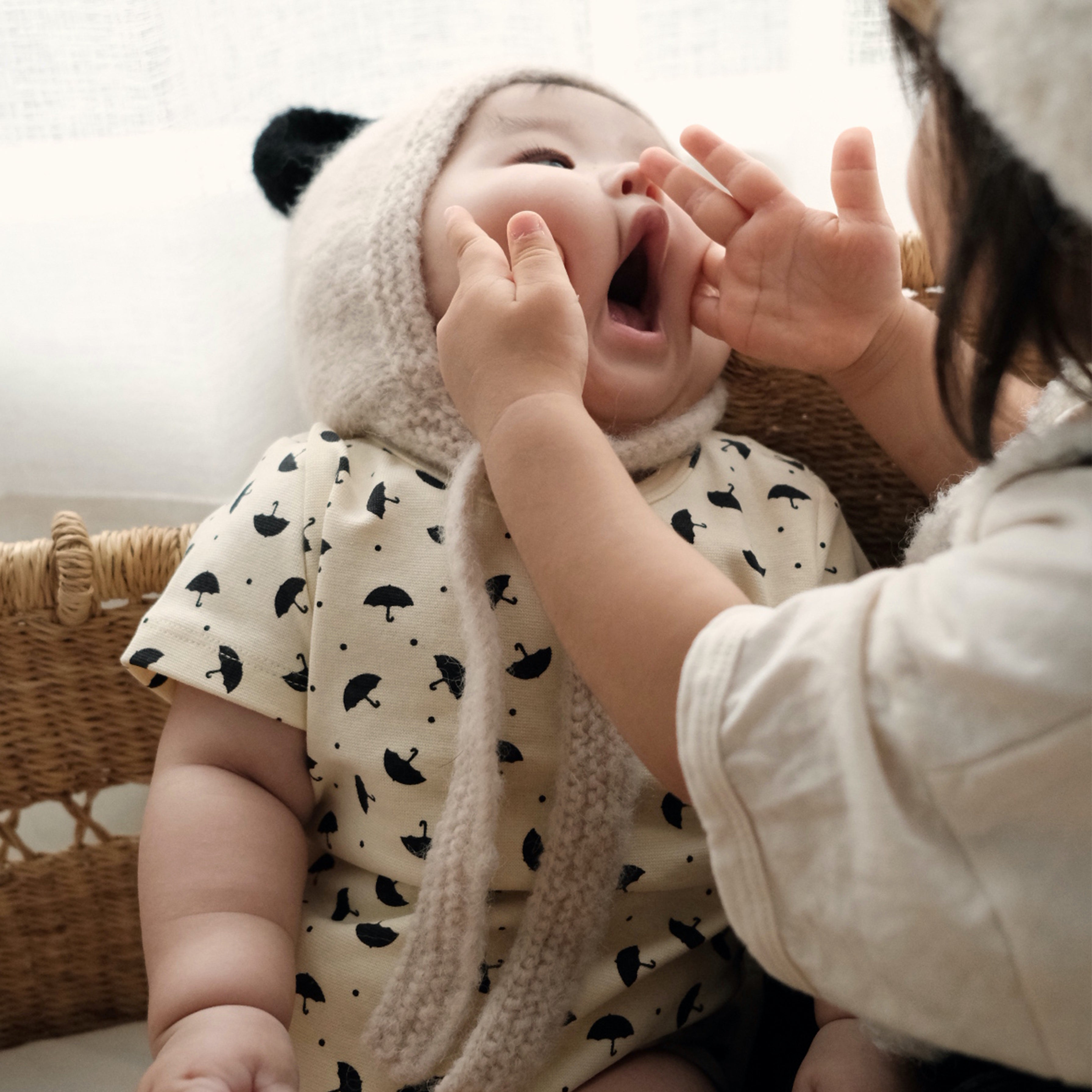 baby wearing the Panda Bonnet, a hand knit baby alpaca hat, laughing while being held.