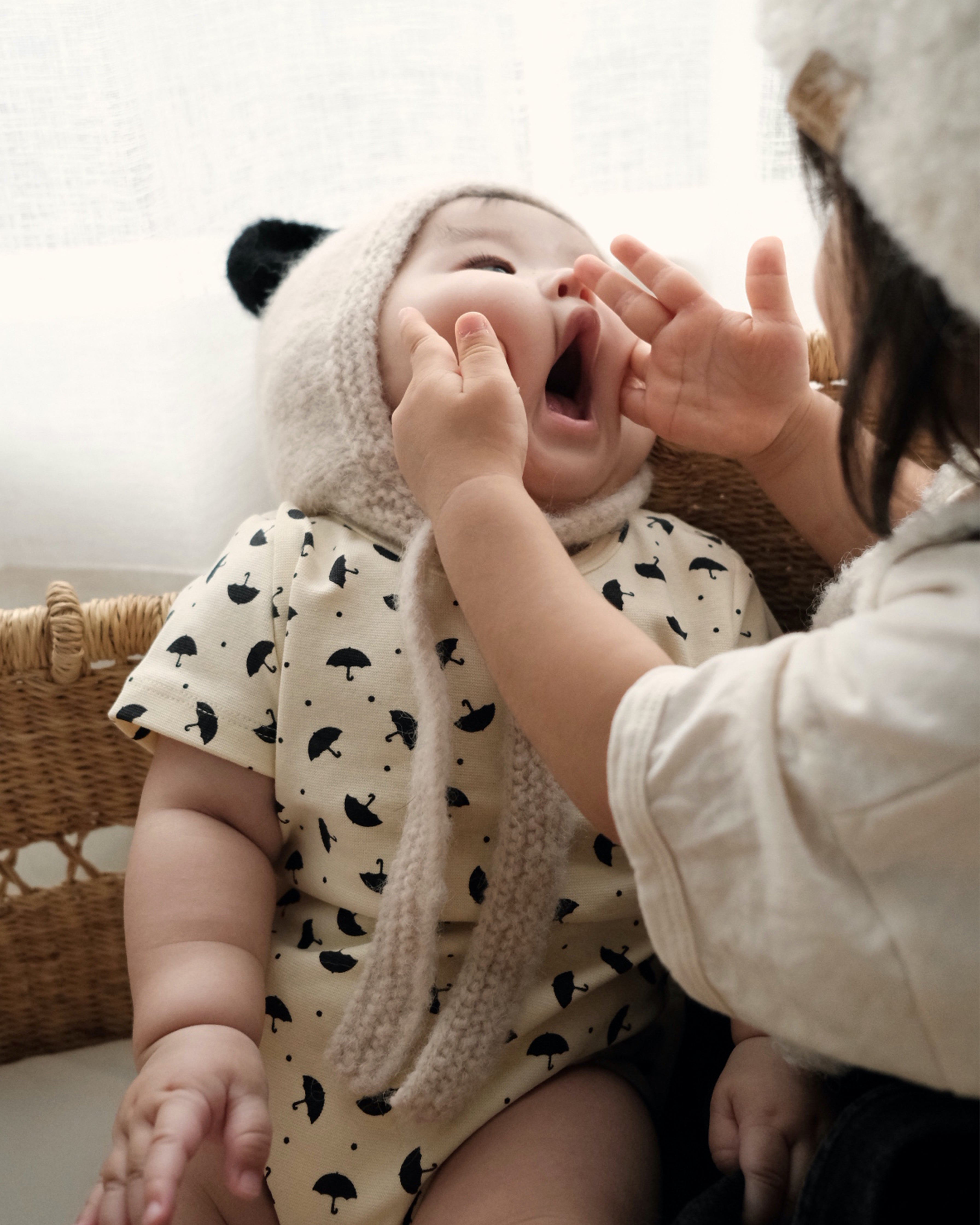  baby wearing the Panda Bonnet, a hand knit baby alpaca hat, laughing while being held.