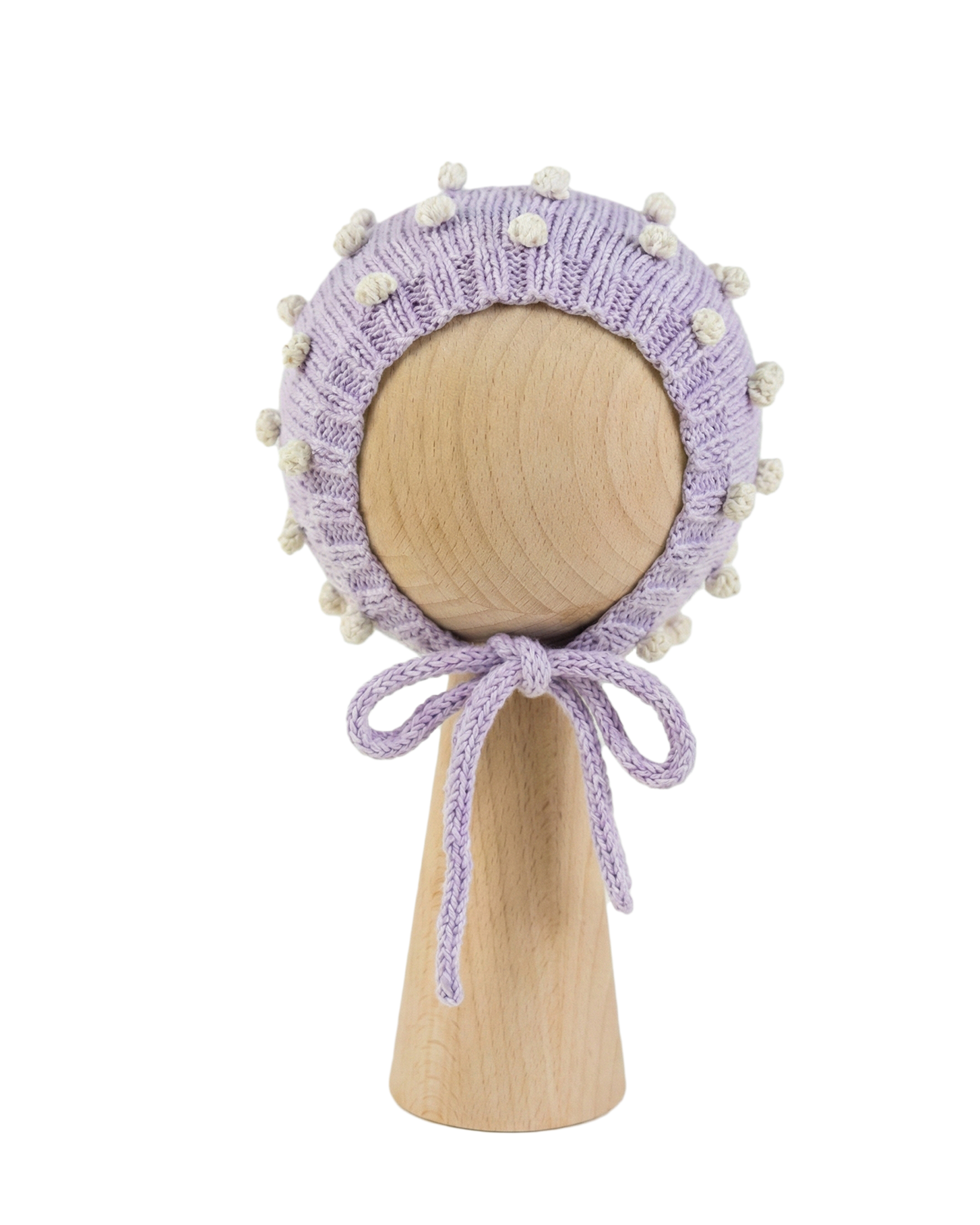 Hand-knitted lavender organic cotton baby bonnet with white popcorn texture on a wooden stand