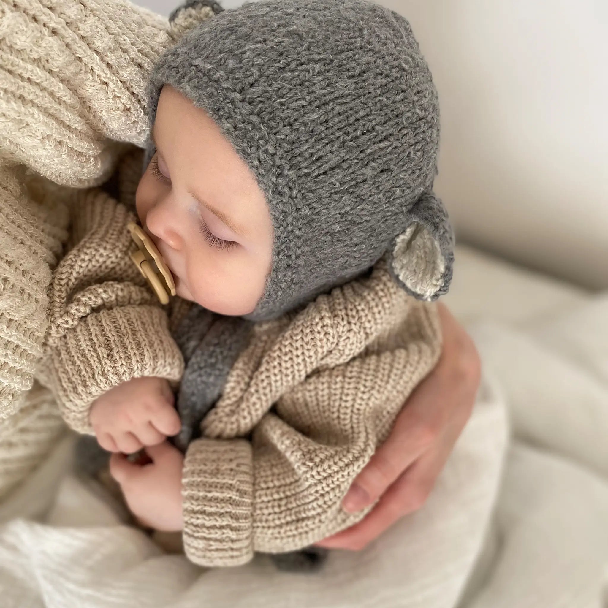 Side view of a baby in the Sheep Bonnet in Charcoal, showing the ecru-lined ear and the knitted tie.