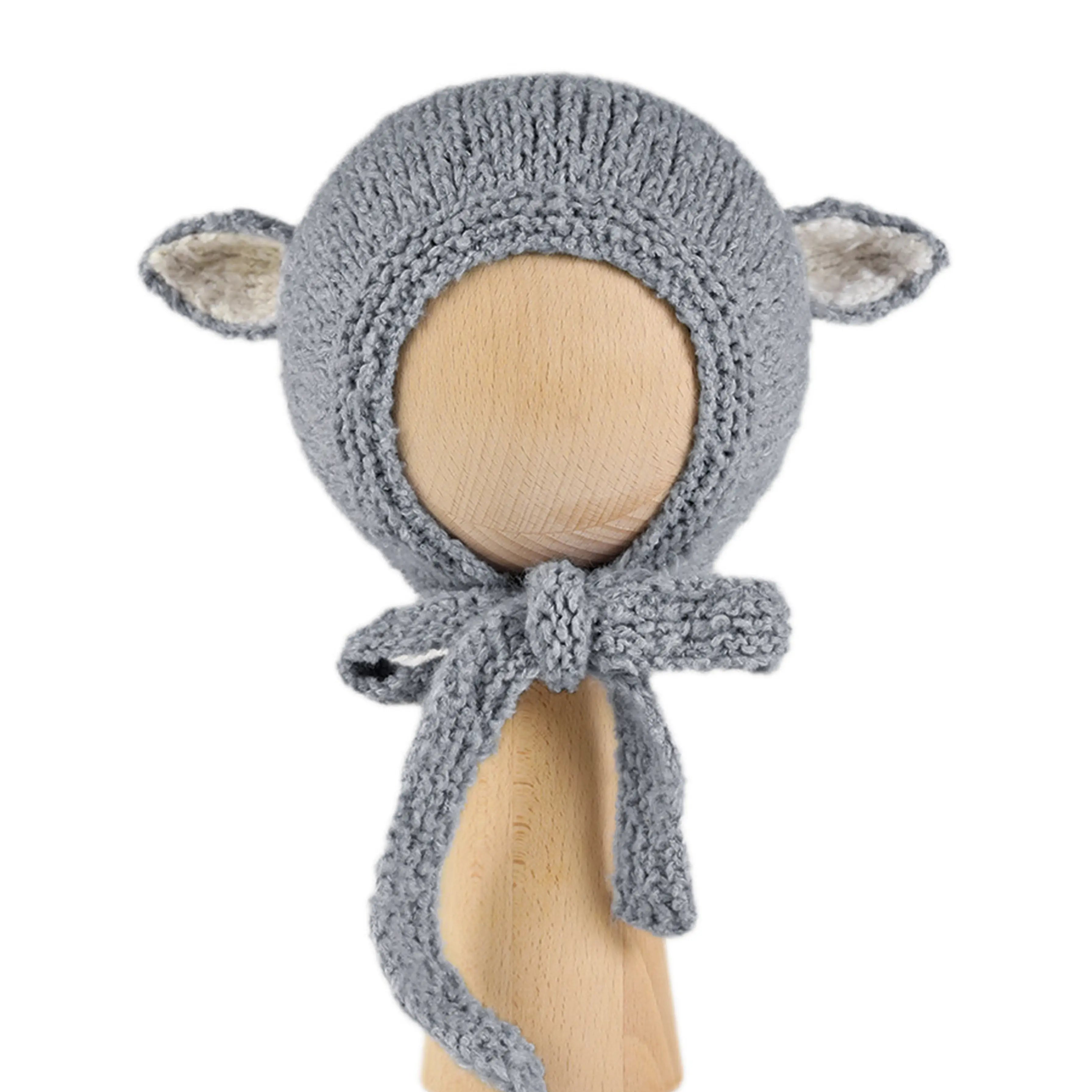 Sheep Bonnet in Charcoal, a knitted cotton bonnet with ecru-lined ears and knitted ties, shown on a wooden display head.