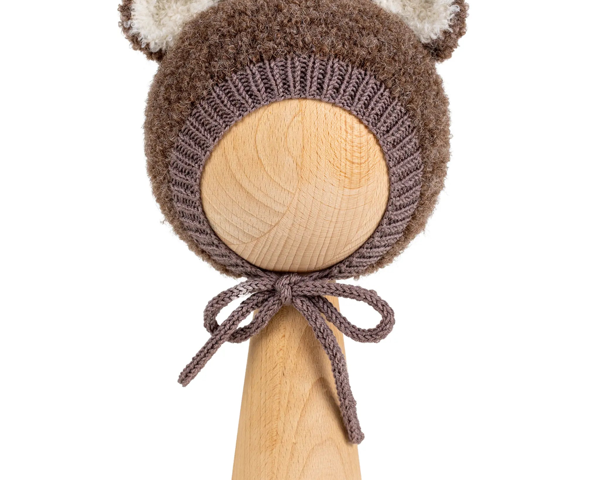 Teddy Bonnet in brown, a knitted baby bonnet with ears in curly bouclé, with cream ear linings and ties under the chin, on a wooden display head.