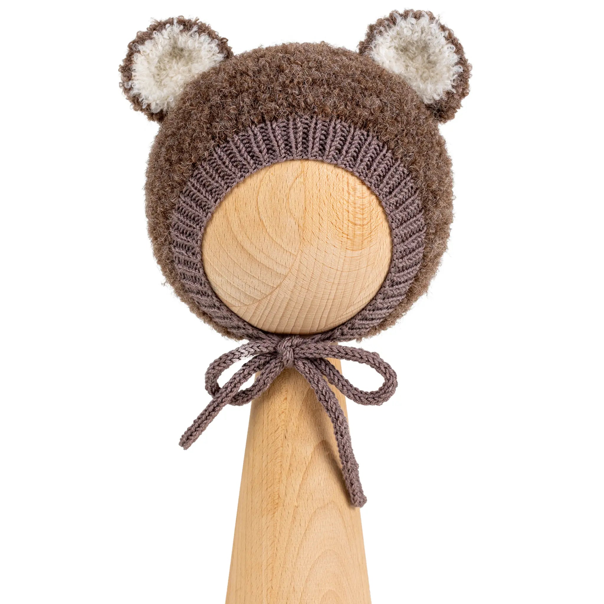 Teddy Bonnet in brown, a knitted baby bonnet with ears in curly bouclé, with cream ear linings and ties under the chin, on a wooden display head.