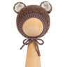 Teddy Bonnet in brown, a knitted baby bonnet with ears in curly bouclé, with cream ear linings and ties under the chin, on a wooden display head.