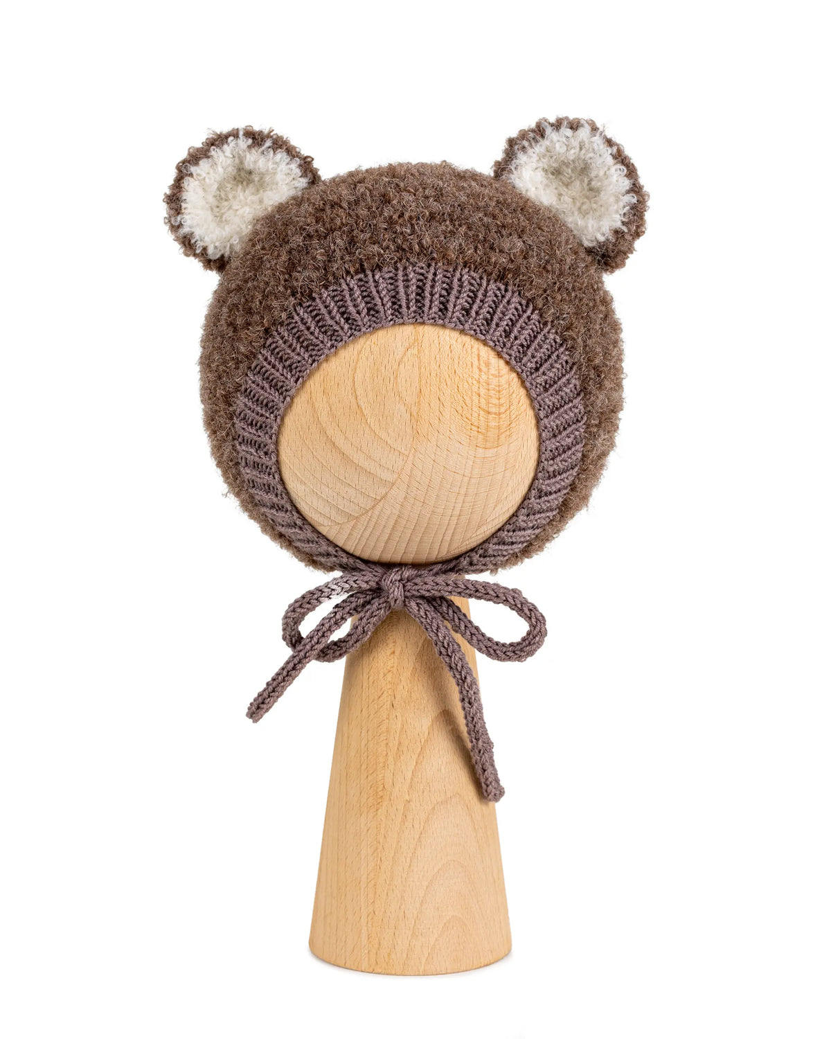 Teddy Bonnet in brown, a knitted baby bonnet with ears in curly bouclé, with cream ear linings and ties under the chin, on a wooden display head.